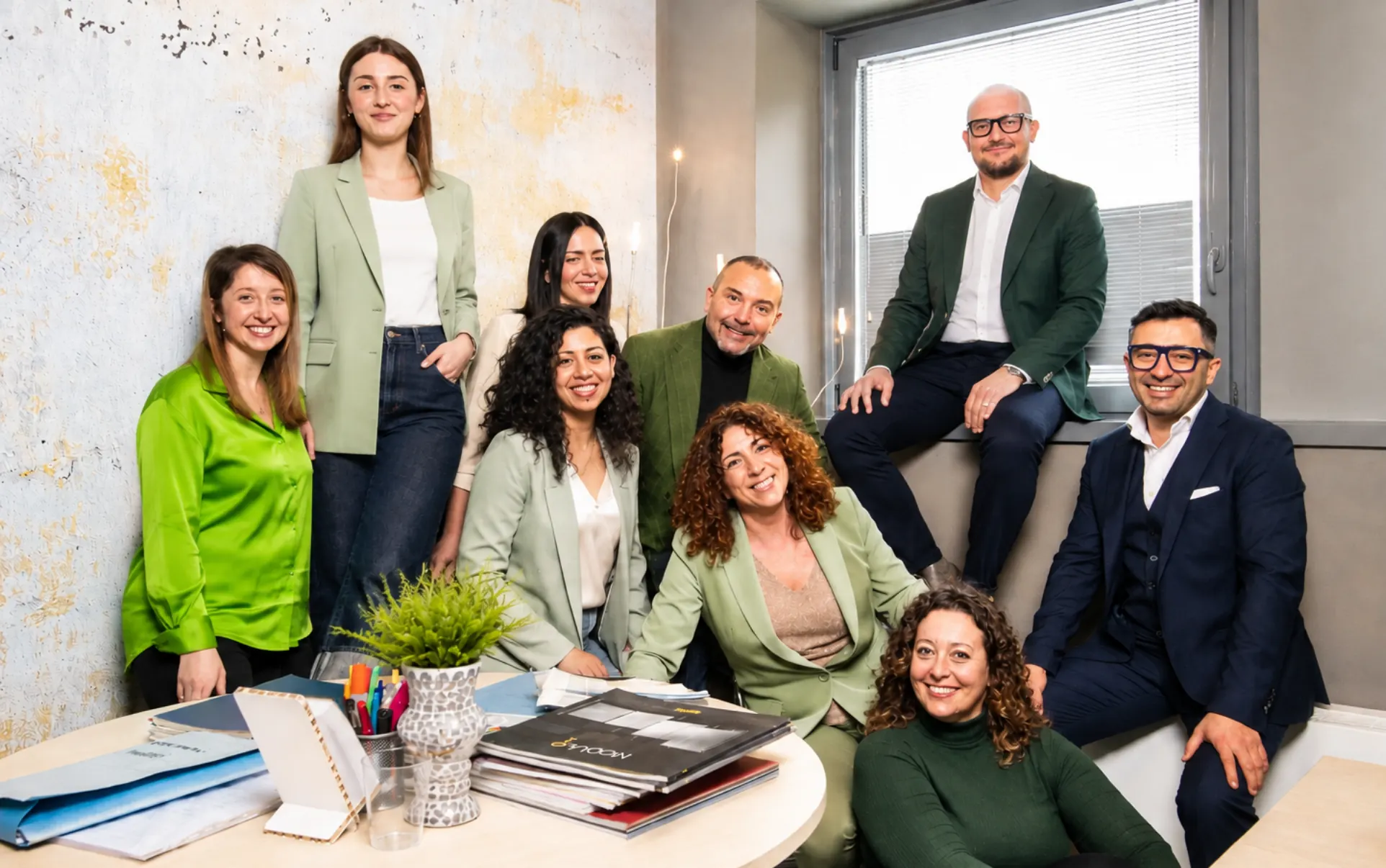 Gruppo di nove persone sorridenti riunite attorno a un tavolo in un ufficio