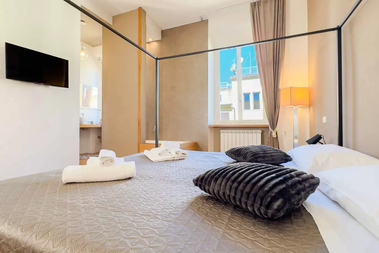 Camera da letto luminosa con letto matrimoniale, asciugamani piegati, tende, TV e lampada