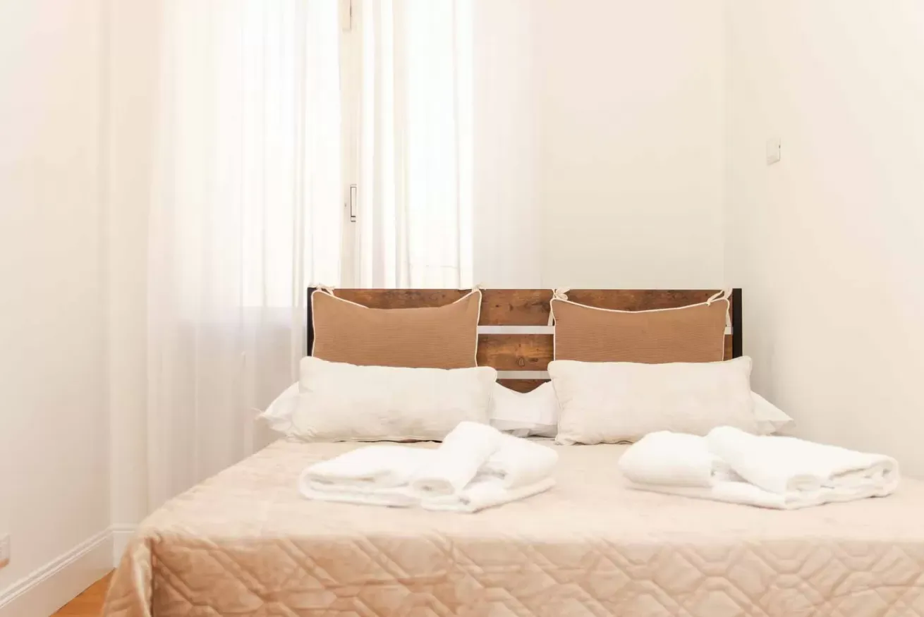Camera da letto luminosa con letto matrimoniale, testiera in legno, cuscini e asciugamani piegati