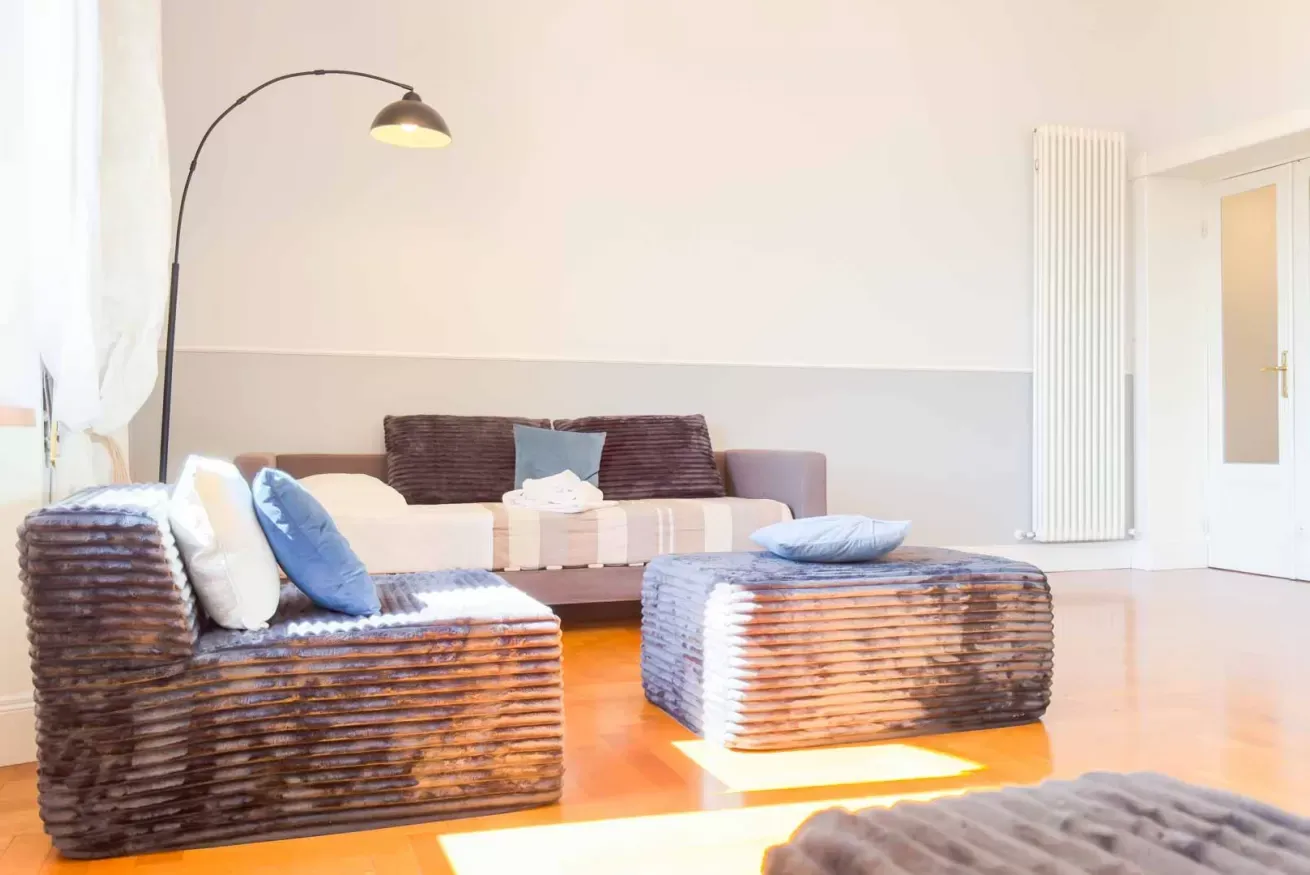 Soggiorno luminoso con divano, poltrona e tavolino imbottiti, lampada ad arco e termosifone