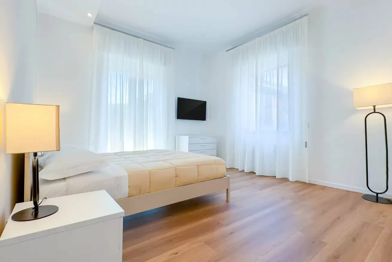 Camera da letto moderna e luminosa con letto matrimoniale, tende bianche, comodini e pavimento in legno