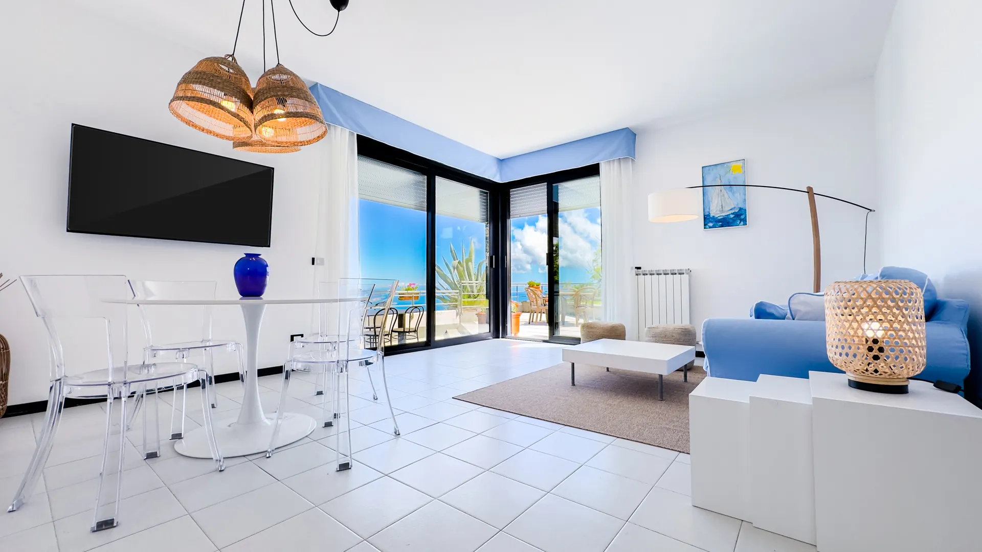 Soggiorno moderno e luminoso con divano blu, tavolo da pranzo, ampie vetrate e vista sul mare