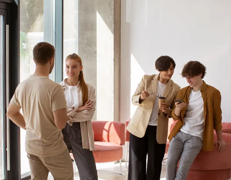 Quattro colleghi parlano in un ufficio luminoso; due consultano uno smartphone