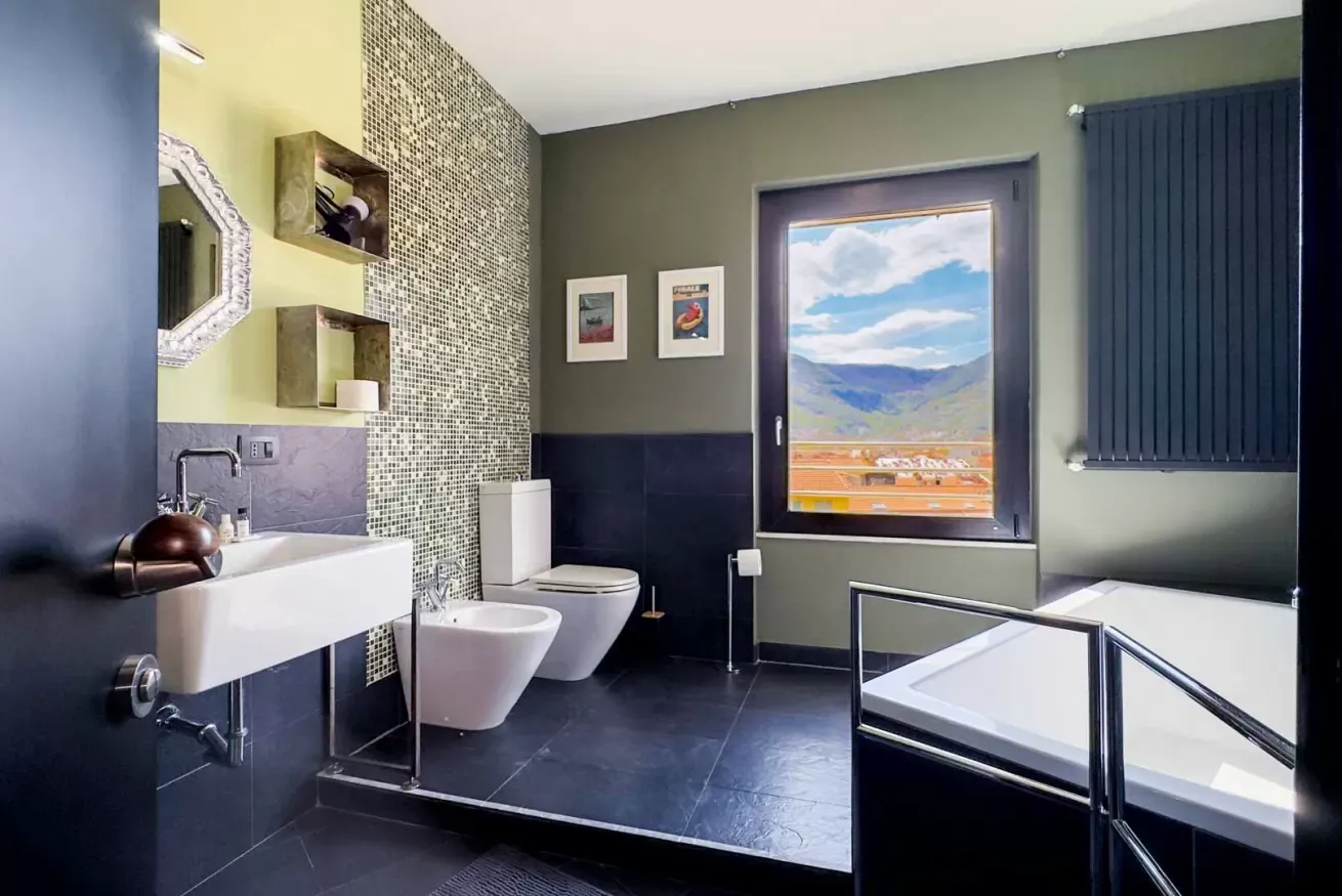 Bagno moderno con lavabo, bidet, WC e vasca da bagno, affacciato su un paesaggio montano
