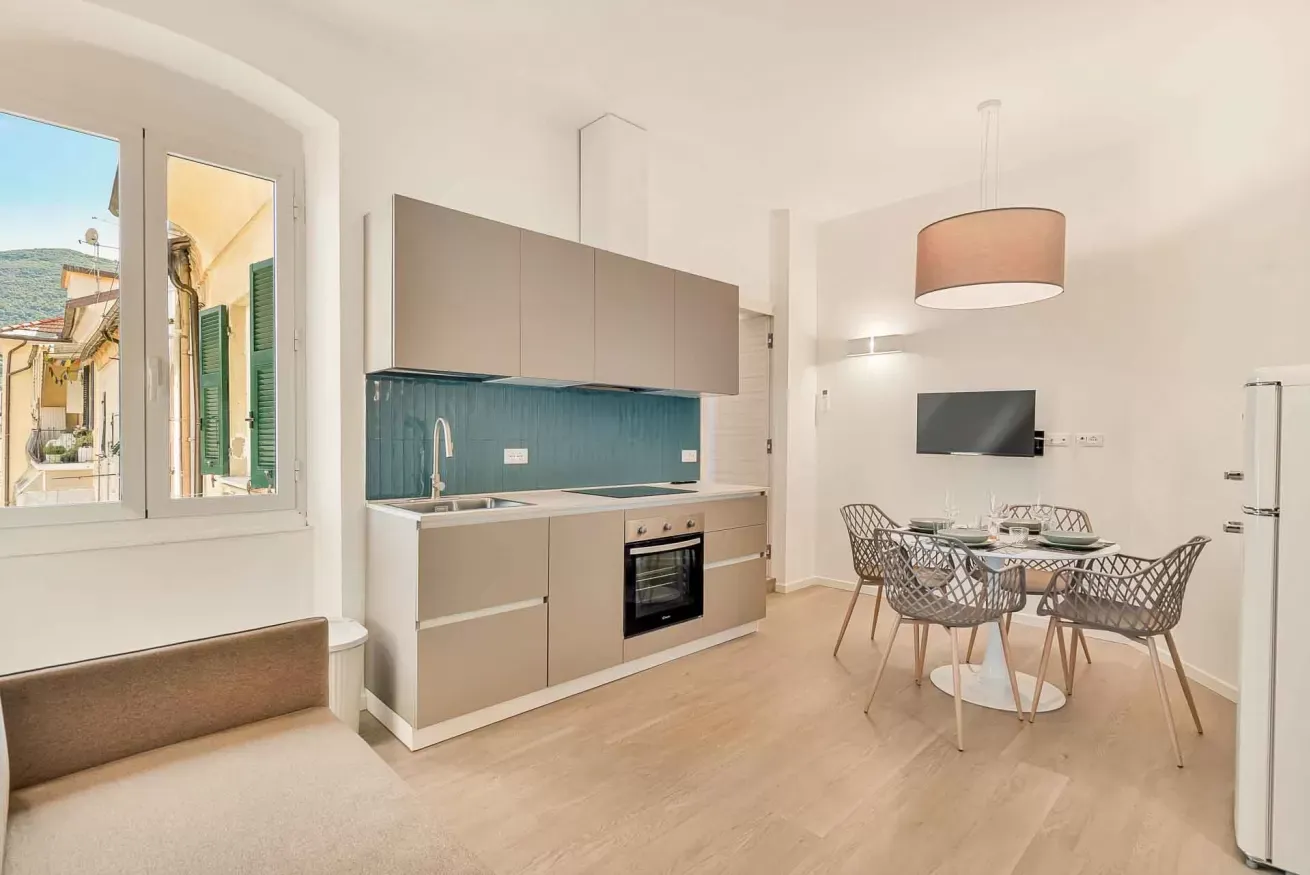 Interno moderno con cucina attrezzata, zona pranzo e divano, illuminato da una grande finestra